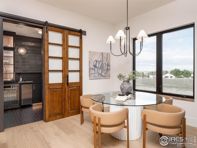 dining room with light hardwood / wood-style floors, a notable chandelier, and a barn door