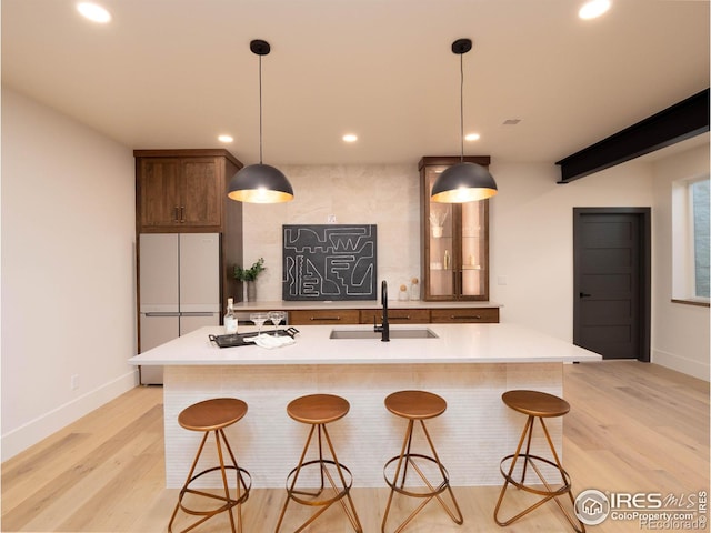 kitchen with an island with sink, light hardwood / wood-style flooring, pendant lighting, sink, and white refrigerator