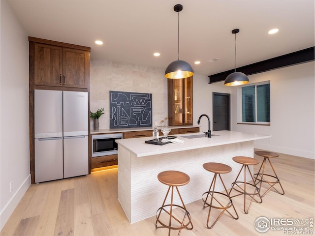 kitchen featuring stainless steel microwave, light wood-type flooring, white fridge, a breakfast bar area, and a center island with sink