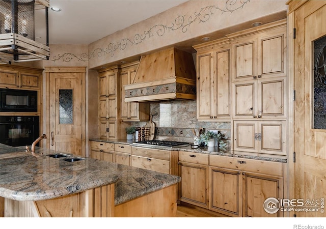 kitchen with dark stone counters, custom exhaust hood, a kitchen island with sink, sink, and black appliances