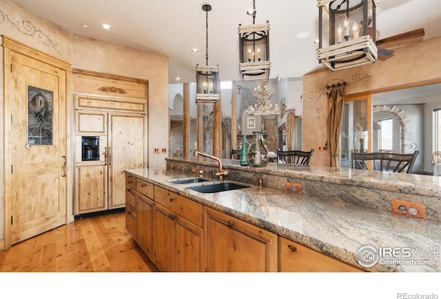 kitchen featuring stone countertops, light hardwood / wood-style floors, sink, and decorative light fixtures