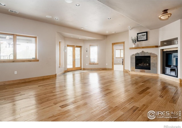 unfurnished living room featuring a fireplace, french doors, and light wood-type flooring