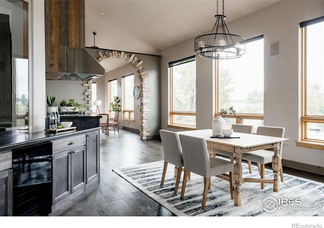 dining room with a healthy amount of sunlight, dark wood-type flooring, beverage cooler, and an inviting chandelier