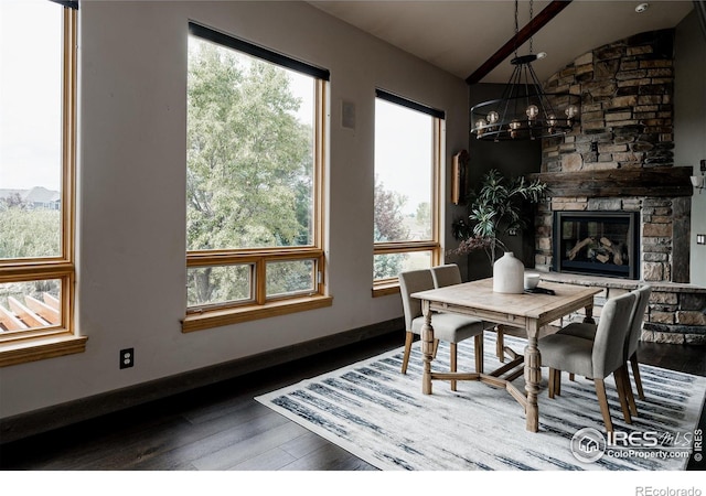 dining room featuring a stone fireplace, a chandelier, wood-type flooring, and lofted ceiling