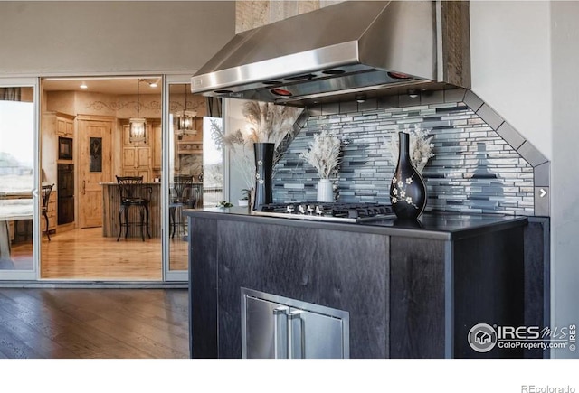 interior space featuring decorative backsplash, stainless steel gas cooktop, wall chimney range hood, decorative light fixtures, and dark hardwood / wood-style floors