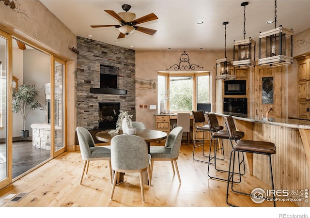 dining room with a stone fireplace, ceiling fan, and light hardwood / wood-style floors