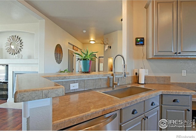 kitchen featuring gray cabinetry, stainless steel dishwasher, dark wood-type flooring, and sink