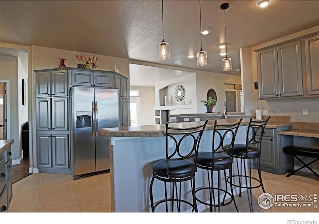 kitchen featuring stainless steel fridge, gray cabinetry, kitchen peninsula, a textured ceiling, and decorative light fixtures