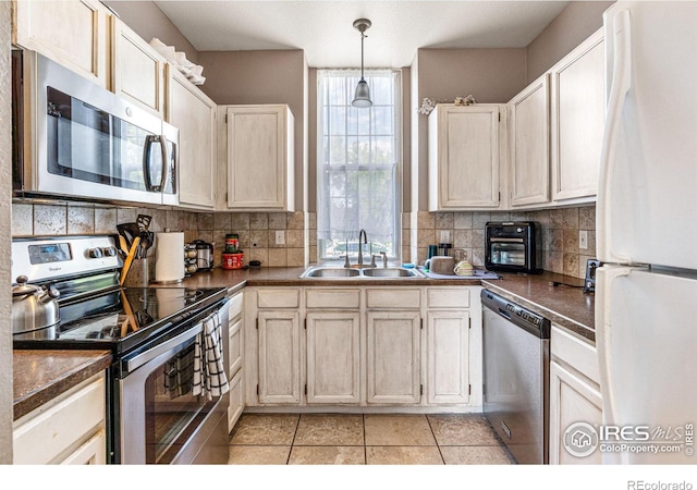 kitchen featuring hanging light fixtures, light tile patterned floors, appliances with stainless steel finishes, sink, and decorative backsplash