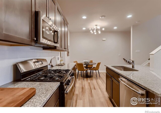 kitchen with light hardwood / wood-style flooring, appliances with stainless steel finishes, light stone countertops, sink, and dark brown cabinetry