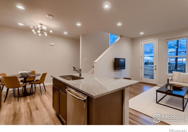 kitchen featuring dishwasher, light hardwood / wood-style flooring, light stone countertops, sink, and a center island with sink