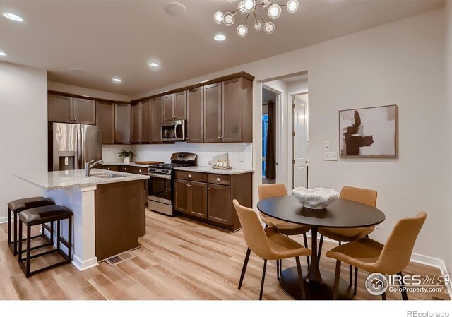 kitchen with light stone countertops, a center island with sink, light hardwood / wood-style flooring, a notable chandelier, and appliances with stainless steel finishes