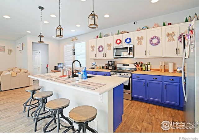 kitchen with white cabinets, blue cabinetry, appliances with stainless steel finishes, sink, and an island with sink