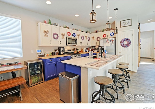 kitchen with stainless steel appliances, white cabinetry, beverage cooler, blue cabinets, and a kitchen island with sink