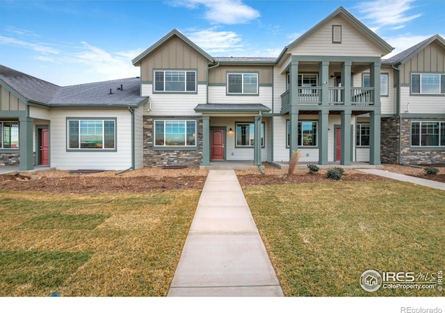 view of front of house featuring a balcony, stone siding, a front lawn, and board and batten siding