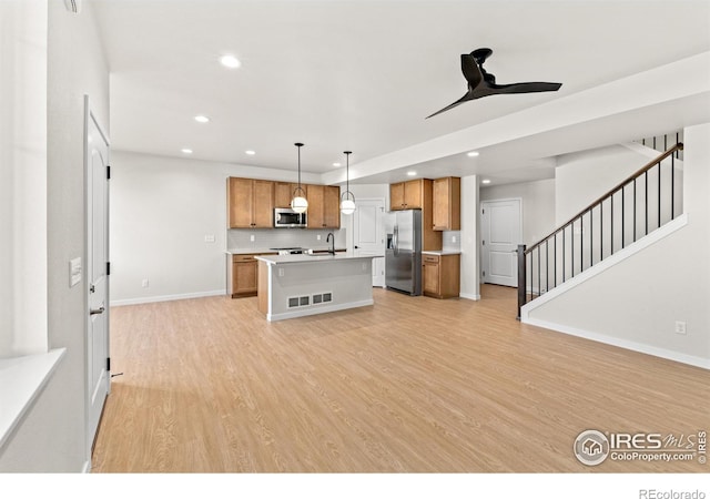 kitchen with appliances with stainless steel finishes, light wood-type flooring, a kitchen island with sink, sink, and decorative light fixtures