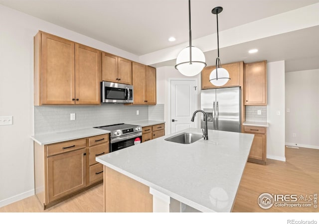 kitchen with a sink, light countertops, appliances with stainless steel finishes, an island with sink, and pendant lighting