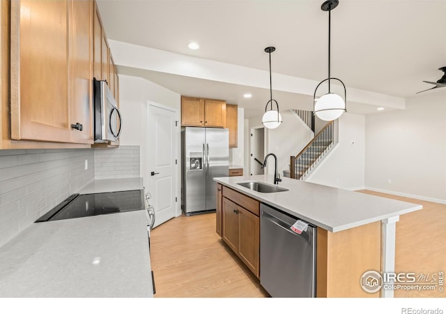 kitchen with appliances with stainless steel finishes, light wood-type flooring, a kitchen island with sink, sink, and hanging light fixtures