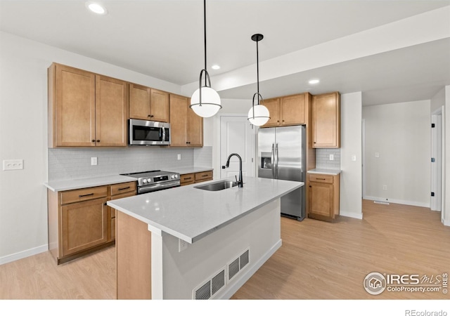 kitchen with stainless steel appliances, light countertops, hanging light fixtures, light wood-style floors, and a sink