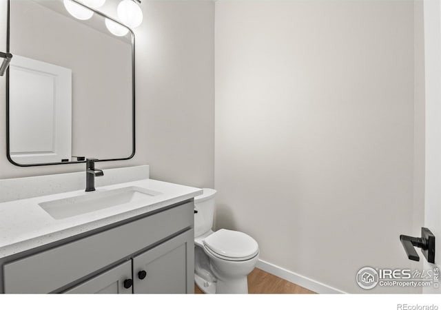 half bathroom featuring toilet, baseboards, wood finished floors, and vanity