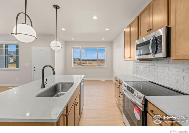 kitchen with sink, hanging light fixtures, appliances with stainless steel finishes, and an island with sink