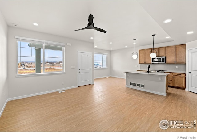 kitchen featuring backsplash, ceiling fan, pendant lighting, light hardwood / wood-style flooring, and an island with sink