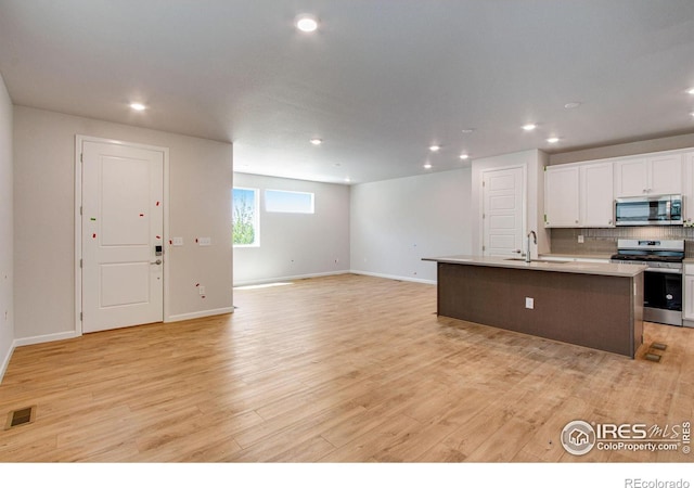 kitchen featuring an island with sink, sink, appliances with stainless steel finishes, white cabinets, and light hardwood / wood-style floors