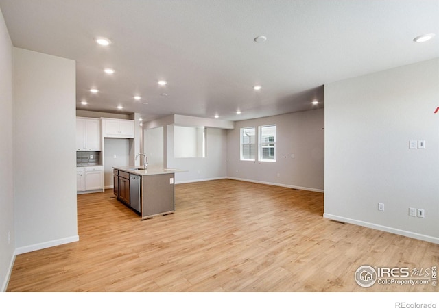 kitchen with light hardwood / wood-style flooring, a kitchen island with sink, stainless steel dishwasher, sink, and white cabinets