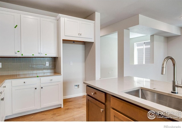 kitchen with sink, backsplash, white cabinets, and light hardwood / wood-style floors