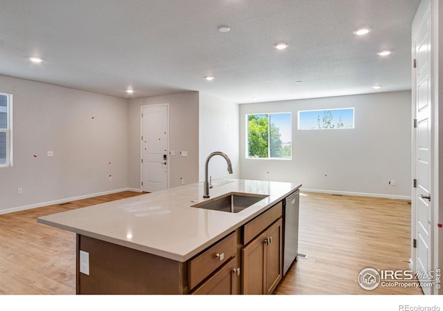 kitchen featuring dishwasher, light wood-type flooring, sink, a center island with sink, and a textured ceiling