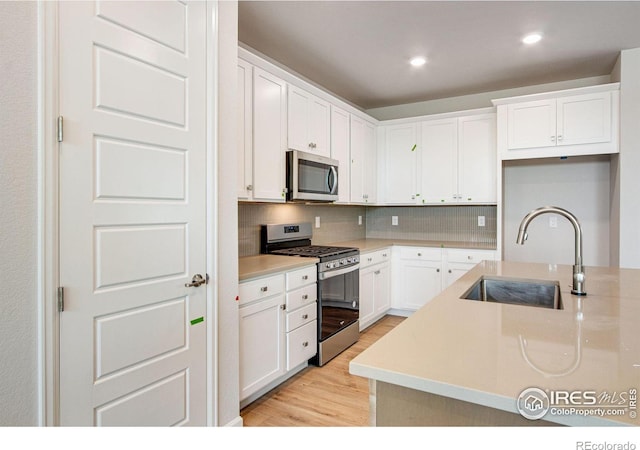 kitchen featuring tasteful backsplash, sink, appliances with stainless steel finishes, white cabinets, and light hardwood / wood-style floors