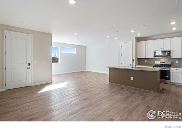 kitchen featuring white cabinetry, light hardwood / wood-style flooring, stainless steel appliances, and a center island with sink