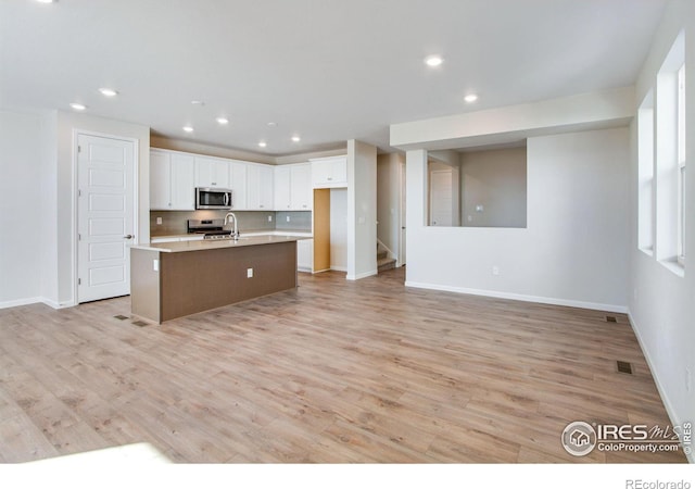 kitchen with an island with sink, appliances with stainless steel finishes, white cabinets, and light wood-type flooring