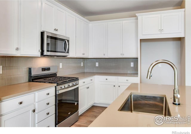 kitchen featuring sink, light wood-type flooring, stainless steel appliances, decorative backsplash, and white cabinets