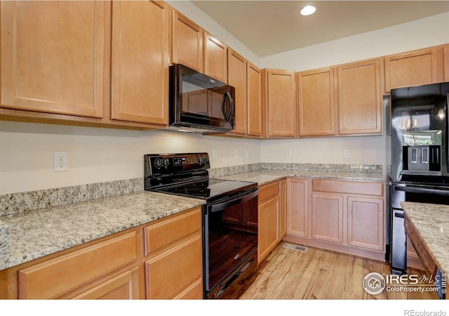 kitchen featuring light brown cabinetry, light stone countertops, light hardwood / wood-style flooring, and black appliances