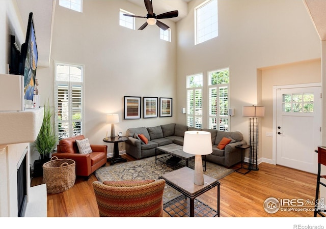 living room with ceiling fan, a high ceiling, and light hardwood / wood-style floors