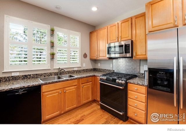 kitchen featuring light wood-type flooring, dark stone countertops, backsplash, stainless steel appliances, and sink