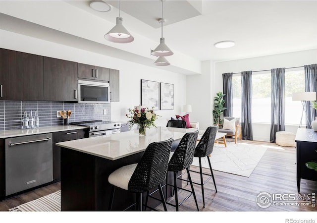 kitchen featuring light wood-type flooring, a kitchen island, stainless steel appliances, and decorative light fixtures