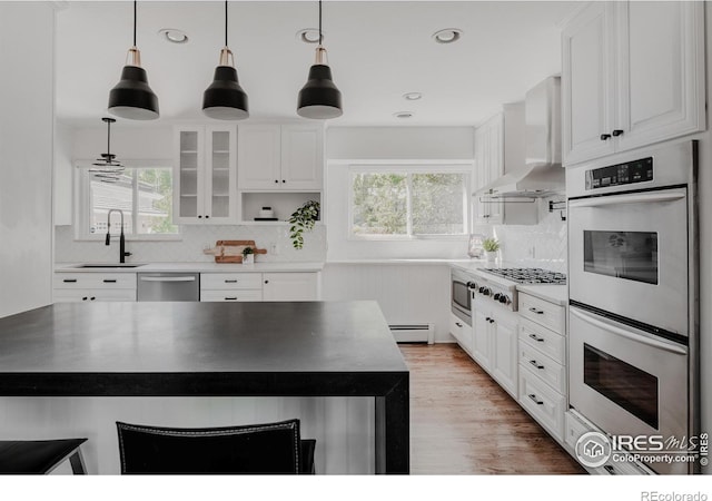 kitchen featuring wall chimney exhaust hood, backsplash, light hardwood / wood-style floors, stainless steel appliances, and white cabinets