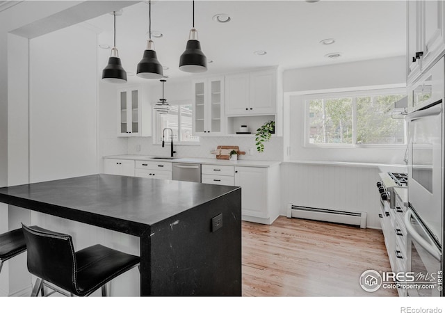 kitchen featuring hanging light fixtures, light wood-type flooring, white cabinetry, a baseboard radiator, and a breakfast bar area