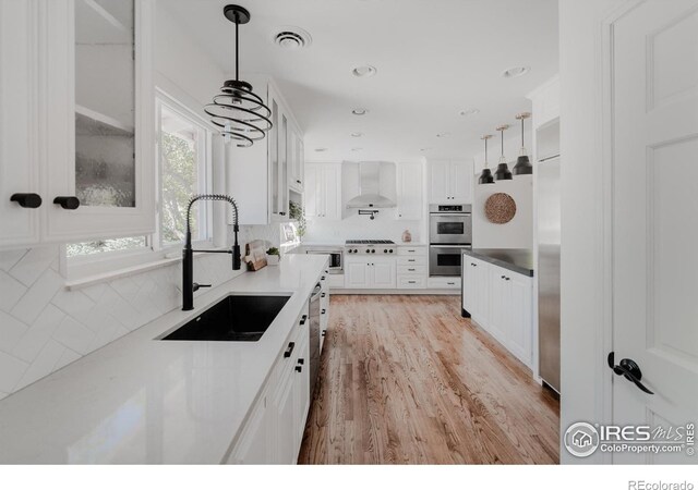 kitchen with stainless steel appliances, sink, decorative backsplash, hanging light fixtures, and wall chimney exhaust hood