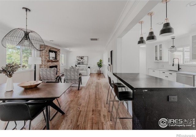 dining area with a fireplace, an inviting chandelier, light hardwood / wood-style flooring, sink, and ornamental molding