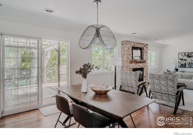 dining area with light wood-type flooring, an inviting chandelier, crown molding, and a stone fireplace