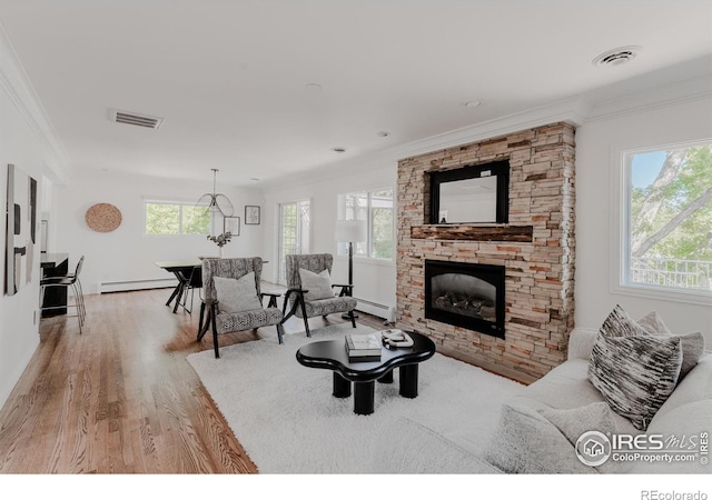 living room with a stone fireplace, wood-type flooring, a baseboard radiator, and a healthy amount of sunlight