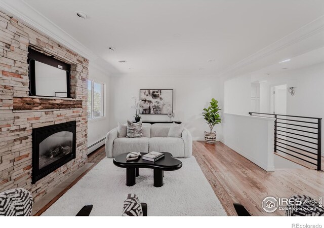 living room featuring crown molding, light hardwood / wood-style flooring, baseboard heating, and a stone fireplace