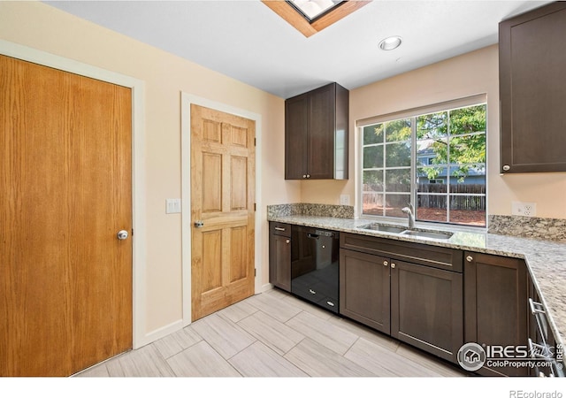 kitchen with light stone countertops, dishwasher, dark brown cabinets, a skylight, and sink