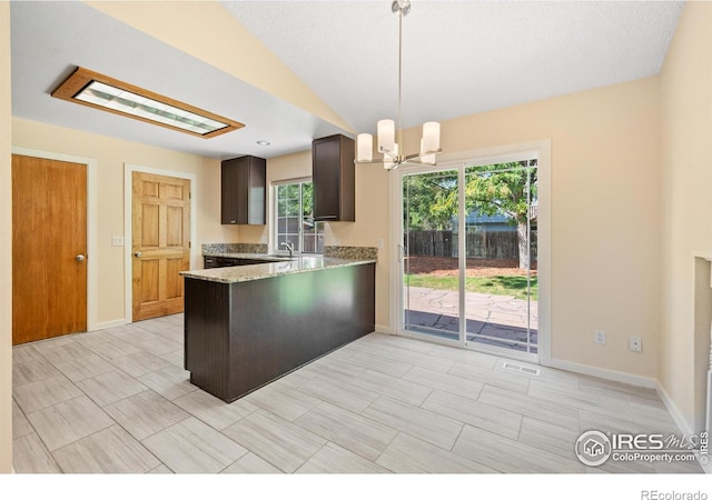 kitchen with dark brown cabinetry, hanging light fixtures, kitchen peninsula, a chandelier, and vaulted ceiling