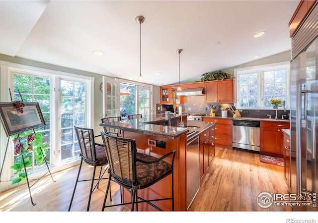 kitchen featuring a breakfast bar, ventilation hood, a center island with sink, appliances with stainless steel finishes, and pendant lighting