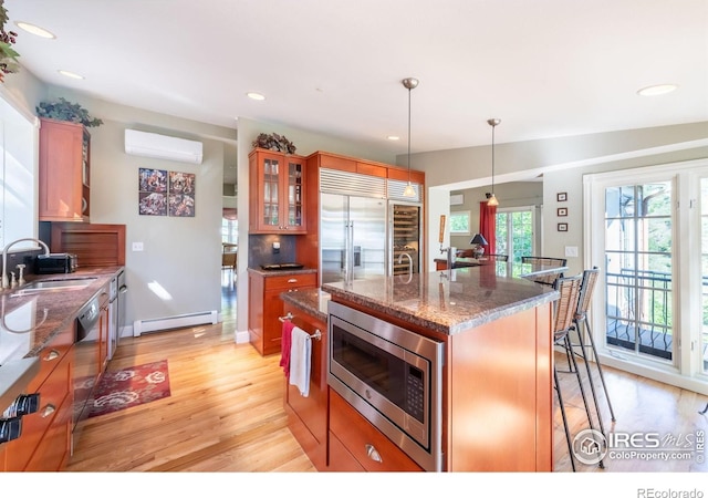 kitchen with sink, built in appliances, decorative light fixtures, a baseboard radiator, and an island with sink