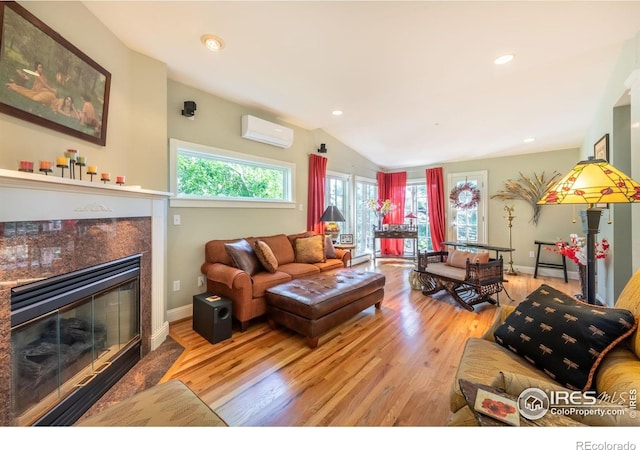 living room featuring vaulted ceiling, a premium fireplace, an AC wall unit, and light hardwood / wood-style floors